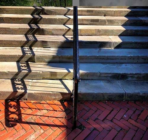 Sunlight creating a zig-zag shadow of a rail on concrete steps